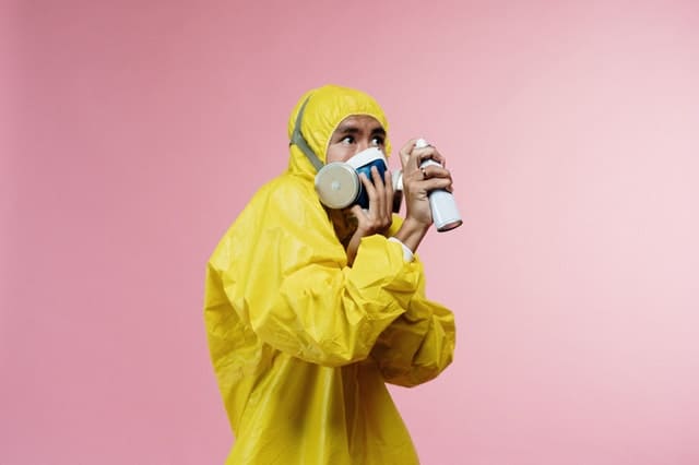 A man in a yellow protective suit with a mask fearfully spraying a sanitizer. 