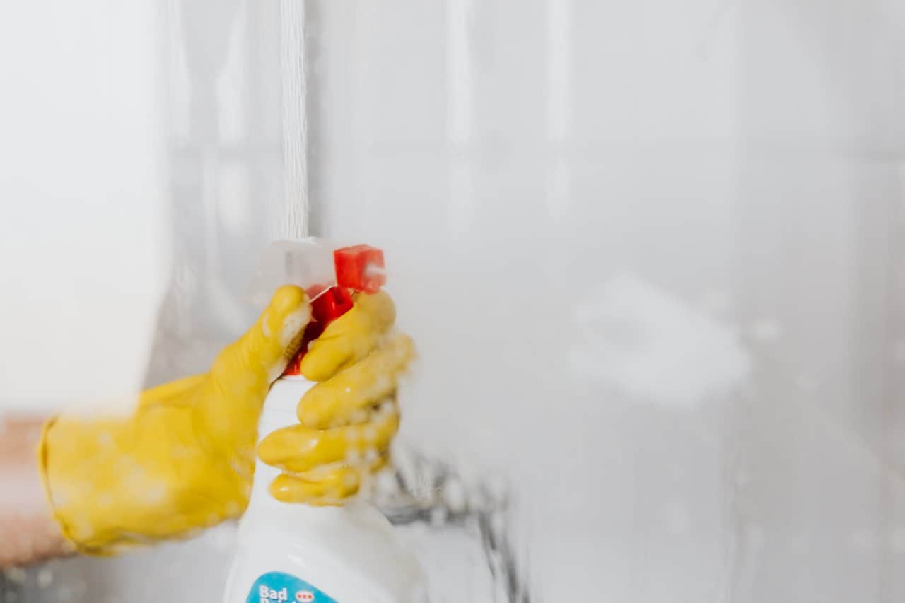 A gloved hand spraying disinfectant on a glass surface.